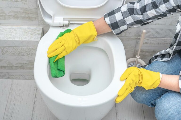 une personne nettoie la cuvette des wc avec des gants et un chiffon