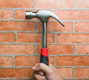 main tient un marteau sur fond de briques