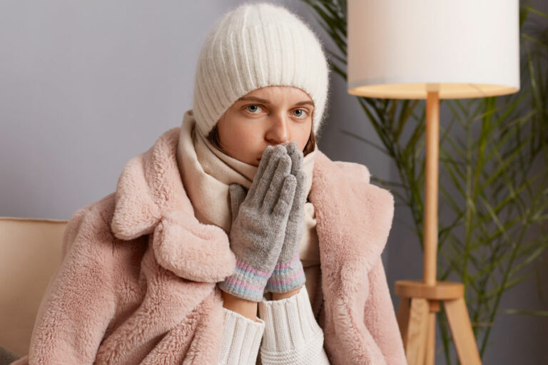 une femme en écharppe pull et gants à froid dans sa maison sans chauffage