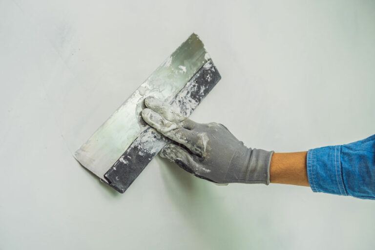 ouvrier applique du mastic au mur enduit par couteau dans une pièce de maison en rénovation
