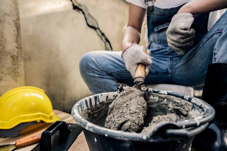 ouvrier manipule le ciment pour des travaux de construction ou rénovation il porte des EPI gants vêtements masque sécurité