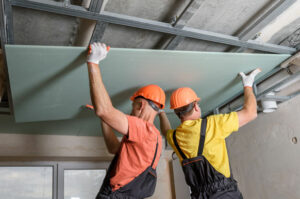 ouvriers du bâtiment portent une plaque de placo pour construire plafond