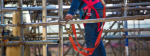 ouvrier du bâtiment accroche le mousqueton de son harnais à son échafaudage pour travailler en hauteur en sécurité et éviter les chutes