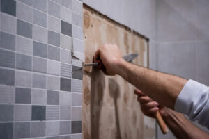 ouvrier du bâtiment carreleur retire le carrelage du mur avec des outils à main : burin et marteau, pour remplacer le revêtement mural de la salle de bains