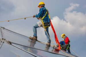 travailleur du bâtiment intervient sur le toit de l'immeuble en construction dans des conditions de travail sécurisées avec un harnais de sécurité et des longes