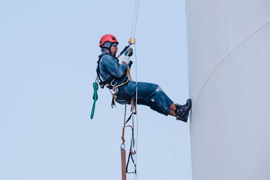 travailleur industriel travaille sur une citerne d'huile, le technicien fait la maintenance sur corde avec un harnais de protection sécurité anti-chute