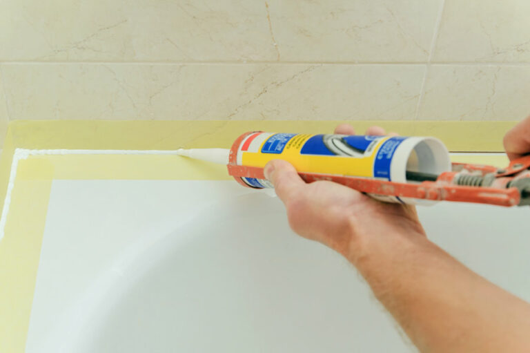 bricoleur pose un joint silicone sur le rebord de la baignoire pour l'étanchéité salle de bains