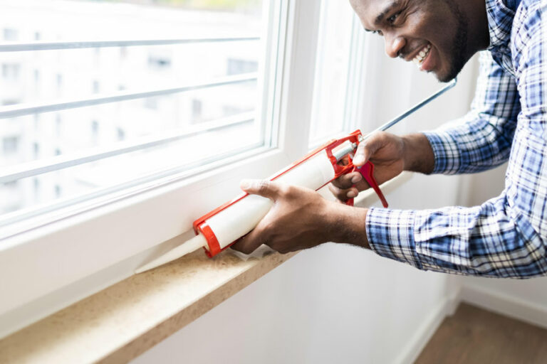 ouvrier pose un joint acrylique sur le bord de la fenêtre pour les finitions