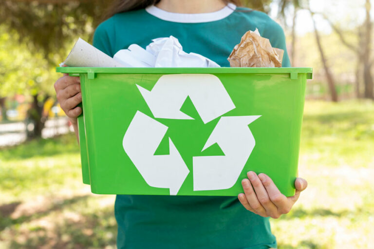 caisse verte de recyclage avec le logo recyclé dessus et des déchets papiers et cartons dedans tenue par une femme