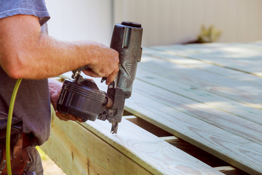 bricoleur utilise un pistolet à clous ou une cloueuse pour fixer les lames de la terrasse en bois