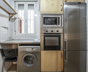 image frontale de la cuisine avec des meubles en bois clair et une colonne d'appareils électroménages en acier inoxydable. avec frigo et lave linge