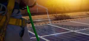 travailleur nettoyant les panneaux solaires photovoltaïques avec une bosse et le jet d'eau du tuyau d'arrosage