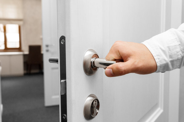 gros plan sur une main qui ouvre la porte en actionnant la poignée. le sens d'ouverture est vers l'extérieur
