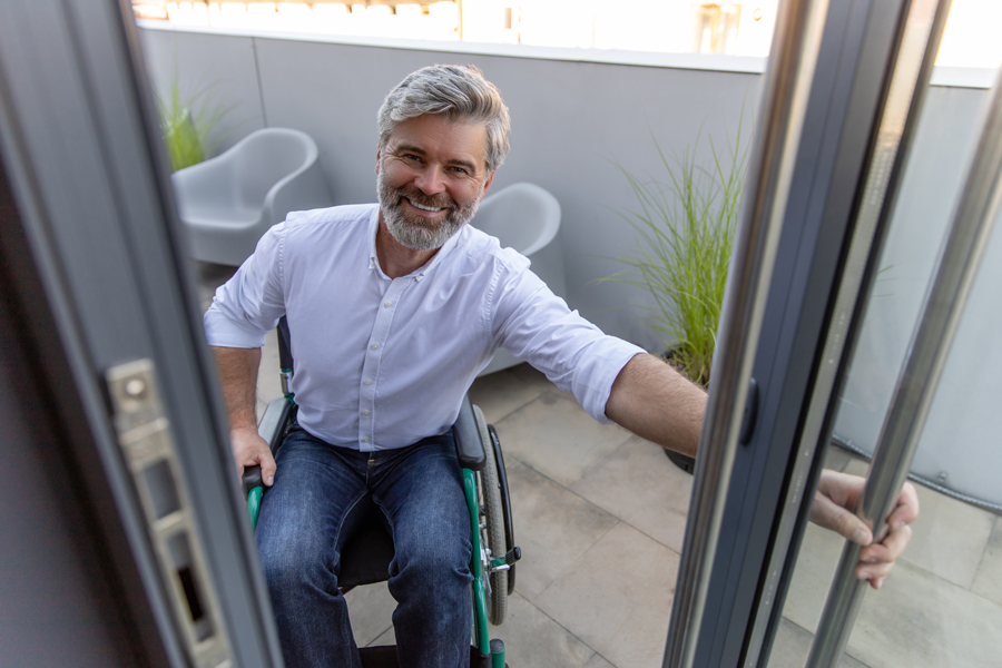 homme barbu grisonnant en fauteuil roulant ouvre la porte PMR