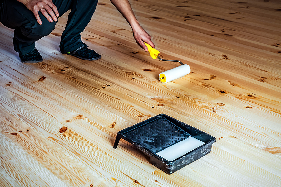 homme vernissant un plancher en bois avec du vitrificateur et un rouleau