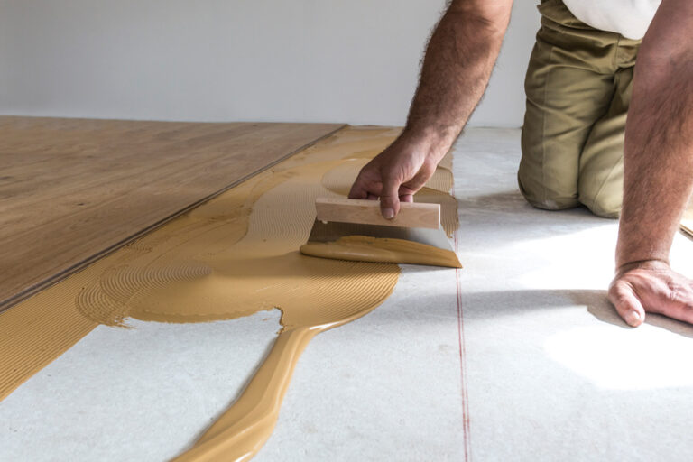 ouvrier pose le parquet en appliquant de la colle liquide sur le sol avec une spatule crantée
