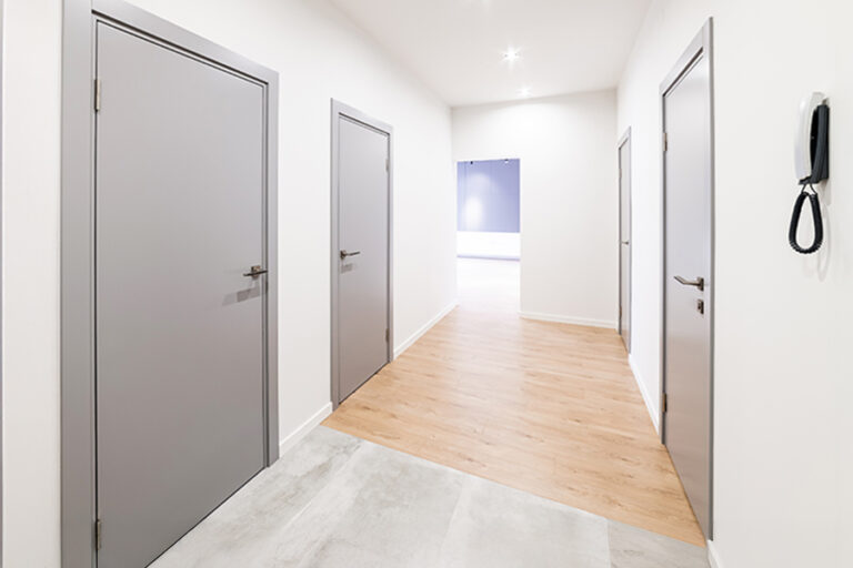couloir blanc dans la maison avec des portes grises et un sol moitié carrelage gris, moitié parquet