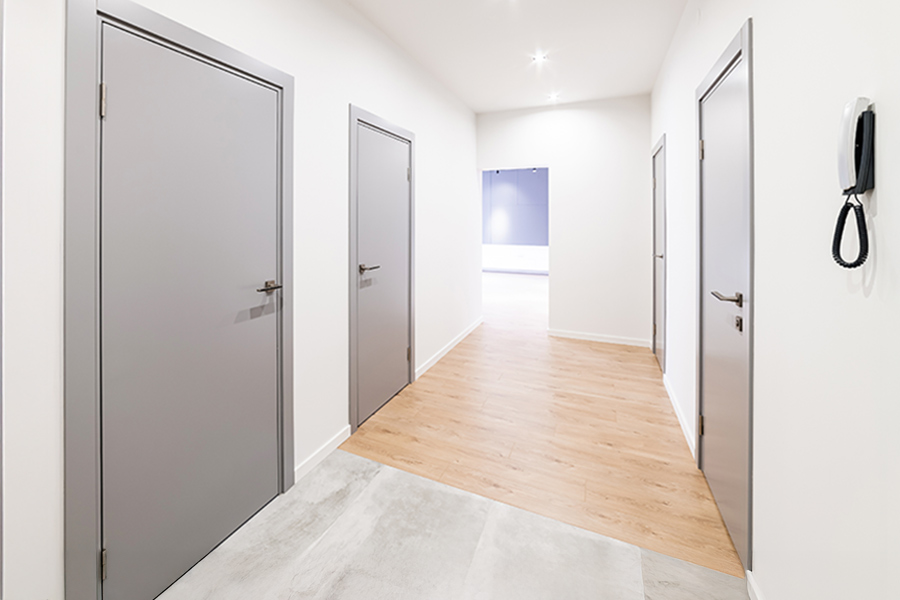 couloir blanc dans la maison avec des portes grises et un sol moitié carrelage gris, moitié parquet