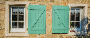 deux fenêtres sur la façade en pierres de la maison ancienne les fenêtres sont posées en feuillure et les volets en bois sont verts