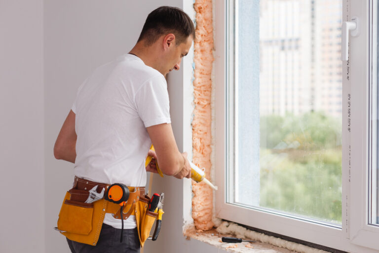 ouvrier pose une fenêtre dans la maison en rénovation, il utilise du mastic pour faire le joint