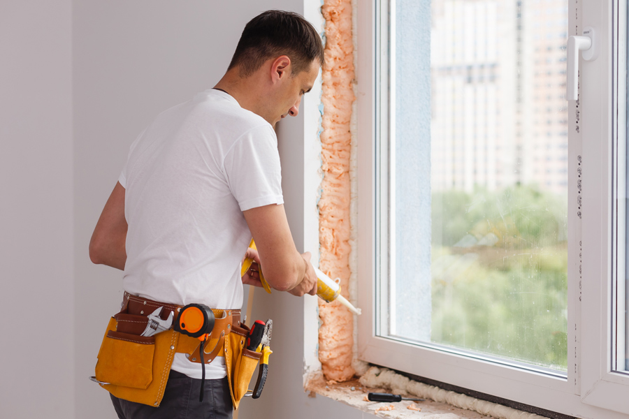 ouvrier pose une fenêtre dans la maison en rénovation, il utilise du mastic pour faire le joint