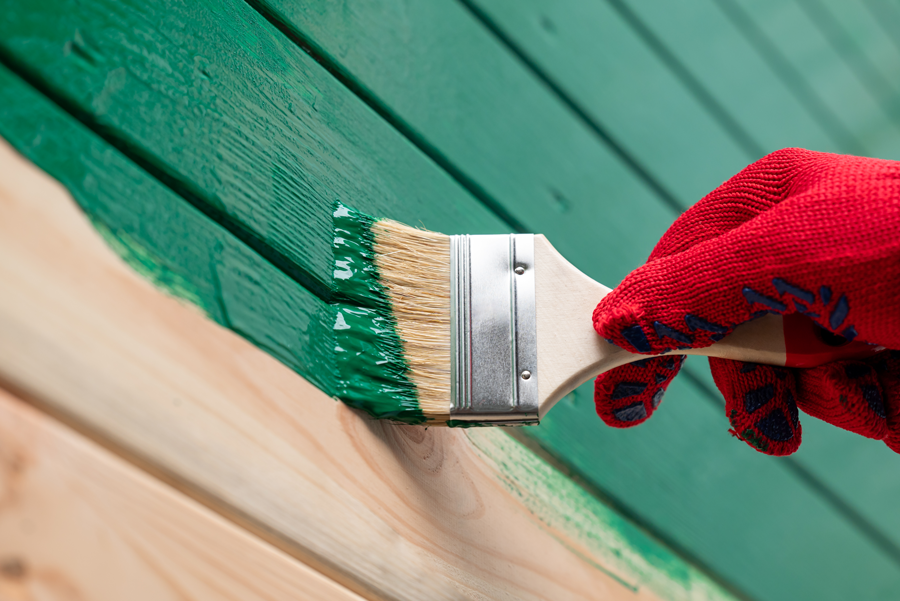 gros plan sur la main gantée qui peint le lambris en bois sur le mur avec un pinceau et de la peinture verte
