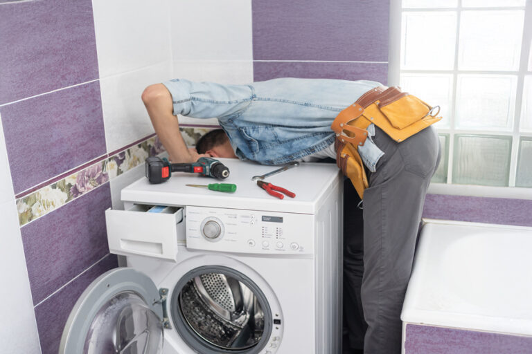 bricoleur penché derrière la machine à laver pour installer ou réparer le tuyau d'évacutaion