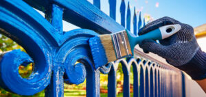 gros plan sur la main qui peint la clôture décorative en fonte avec un pinceau et de la peinture glycero bleue couvrante