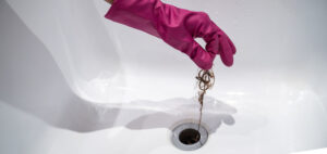 la main porte des gants de ménage et retire les cheveux du siphon de la baignoire